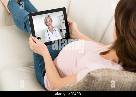Erwartung liegende Frau auf Sofa Videokonferenzen mit Arzt auf Digital Tablet Stockfoto