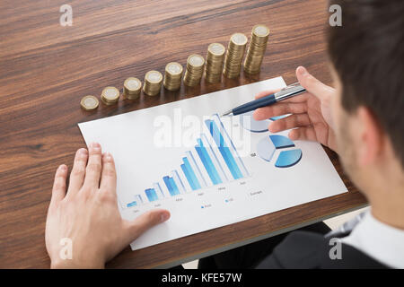 Nahaufnahme der Geschäftsmann Analyse der Grafik vor gestapelte Münzen Stockfoto