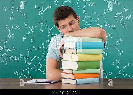 Traurige junge Mann lehnte sich auf Stapel Bücher auf dem Schreibtisch Stockfoto