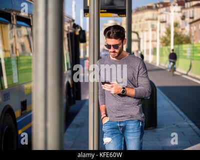Mann mit Phone an der Haltestelle Stockfoto