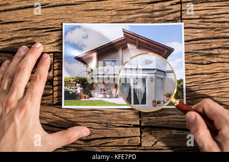 Nahaufnahme einer Person suchen Haus Foto durch die Lupe über dem Schreibtisch aus Holz Stockfoto