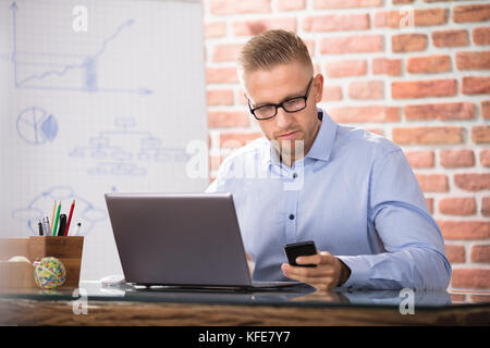 Geschäftsmann mit Brillen mit Smart Phone während der Arbeit im Büro Stockfoto