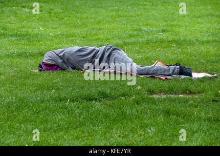 Schlafende obdachlose Person in eine graue Decke auf Gras gewickelt Stockfoto