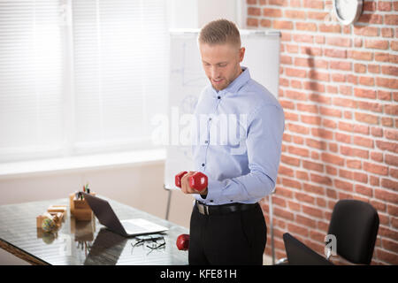 Attraktive Geschäftsmann Trainieren mit einem roten Hanteln in Office Stockfoto