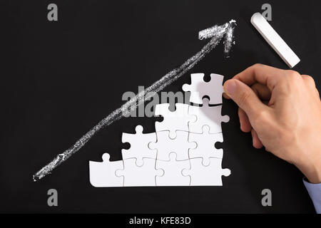 Nahaufnahme einer Person, die die Weißen Rätsel gegen nach oben zeigenden Pfeil auf der Tafel Stockfoto