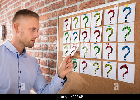 Close-up ein Geschäftsmann mit Fragezeichen auf Notizen über Bulletin Board befestigt Stockfoto