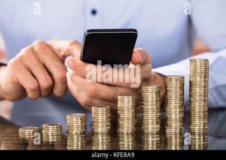 Stapel von zunehmenden Münzen vor der Geschäftsmann mit Smart Phone für die Berechnung der Münzen Stockfoto