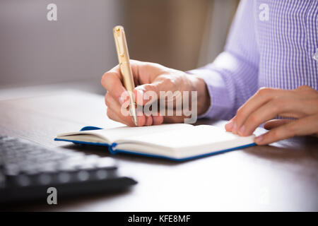 Geschäftsmann schreiben auf Tagebuch mit der Goldenen Feder auf dem Schreibtisch am Arbeitsplatz Stockfoto