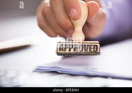 Nahaufnahme einer Person hand Stempel auf Dokument über den Schreibtisch im Büro genehmigt Stockfoto