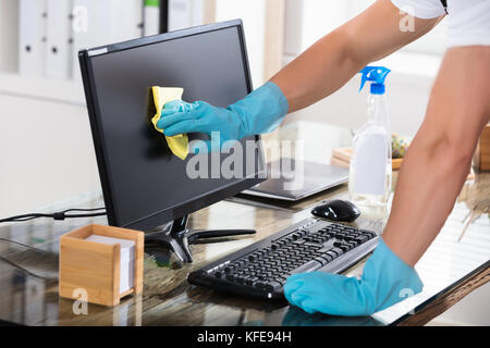 In der Nähe von einem Hausmeister Hand Handschuhe Reinigung Computer Bildschirm mit Rag Stockfoto