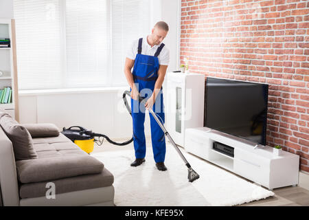 Lächelnden jungen männlichen Hausmeister saugen Teppich zu Hause Stockfoto