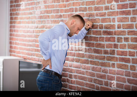 Junger Mann lehnte sich an die Wand berühren den Rücken Schmerzen Stockfoto