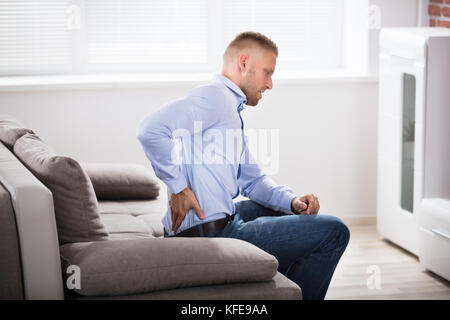 Mann sitzt auf einem Sofa mit Rückenbeschwerden zu Hause Stockfoto