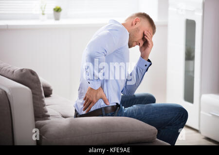 Unglückliche junge Mann sitzt auf einem Sofa leiden unter Kopfschmerzen. Stockfoto