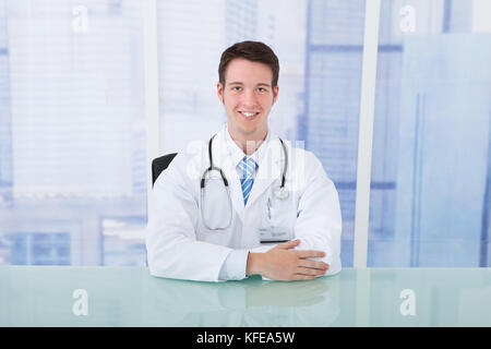 Portrait von jungen männlichen Arzt sitzen am Schreibtisch, in der Klinik Stockfoto