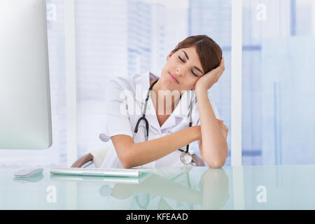 Junge Frau Doktor am Schreibtisch im Krankenhaus müde Stockfoto