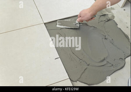 Festlegung der Keramikfliesen. Troweling Mörtel auf Betonboden in der Vorbereitung für die Verlegung von weißen Bodenfliesen. Stockfoto