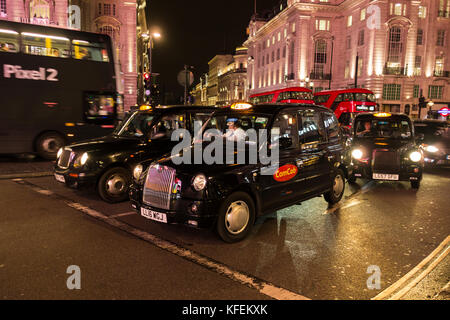 Schwarze Londoner Taxis warten auf die Ampelwechsel an einem überfüllten Piccadilly Circus, London, England, Großbritannien Stockfoto