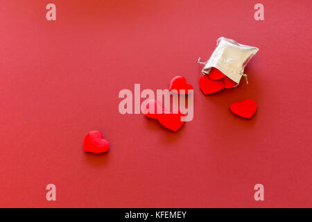 Nahaufnahme eines kleinen Glänzendes Silber Tasche mit niedlichen roten Samt Herzen auf rotem Hintergrund gefüllt. Konzept der romantischen Liebe Geschenk für Paare, Valentines Tag Stockfoto