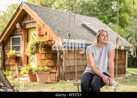 Tausendjährigen Frau im Hinterhof sitzen auf Swing mit Glas Wein denken Stockfoto