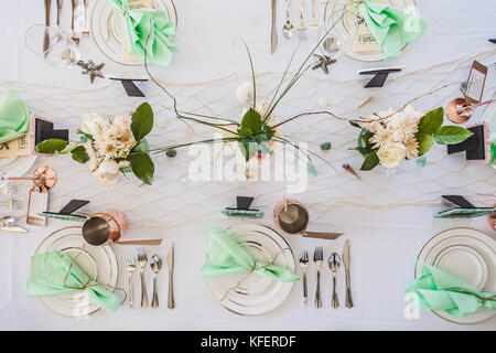 Elegante Strand themed Hochzeit Tischdekoration mit mint grün Servietten und Kupfer Akzent Tassen. verstreute Muscheln und Sterne auf Fischnetz Tabelle Runner. Stockfoto