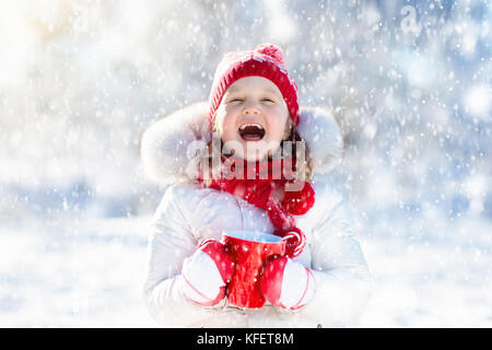 Kind trinken heiße Schokolade mit Marshmallows in schneereichen Winter Park. Kid mit Tasse warmen Kakao trinken zu Weihnachten Urlaub. kleine Mädchen spielen in Sn Stockfoto