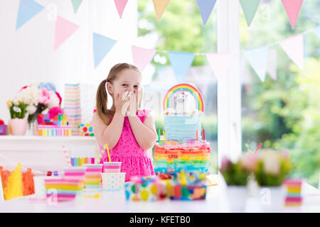 Kindergeburtstag mit farbenfrohen Pastelltönen dekoriert und Einhorn rainbow Kuchen. Kleines Mädchen mit Süßigkeiten, Süßigkeiten und Obst. Ballons und Banner bei festlichen Stockfoto