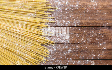 Spaghetti Teigwaren auf einem hellbraun Holz- Oberfläche, mit viel Weizen Mehl bestreut oben und Um Stockfoto