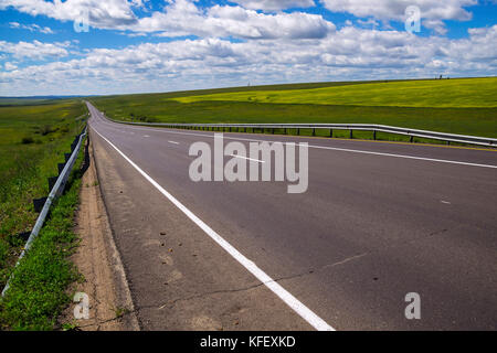 Die asphaltierte Straße im Sommer die Wiesen unter blauen Himmel mit weißen Wolken Stockfoto