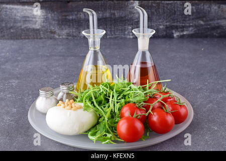 Zutaten für die traditionelle italienische Caprese Salat auf einem Glas Fach auf grauem Hintergrund mit Flaschen Olivenöl und Weinessig. Stockfoto