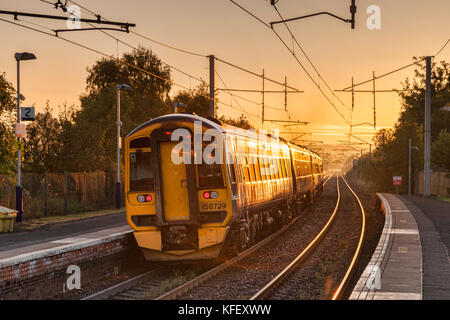 Früher Zug verlässt Bahnhof mit Sonne scheint auf ihn. Stockfoto