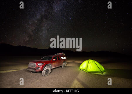 Ein rotes Fahrzeug und Grünen camping Zelt Glühen von Licht im Inneren. Bis auf einer flachen, trockenen lakebed mit den Nachthimmel und Milchstraße Overhead. Stockfoto