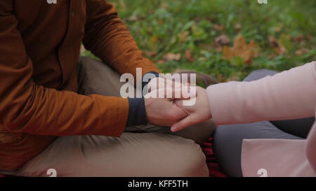Junge Paare sitzen zusammen in einem Sommerpark und machen ein Picknick auf einer karierten Picknickdecke. Pärchen im Park, die auf dem Gras sitzen, gute Zeit zusammen. Ein Paar, das sich auf dem Gras entspannt Stockfoto