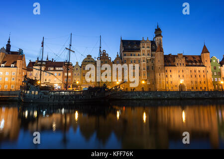 Malerischer Blick auf eine touristische Segelboot und beleuchteten alten Gebäuden entlang der langen Brücke am Wasser in der Stadt in Danzig, Polen, am Abend. Stockfoto