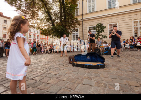 Ein junger unbekannter Mädchen Uhren eine Brass Band zu einer großen Menschenmenge in Rynok (Markt) Square, Lemberg, Ukraine durchführen Stockfoto
