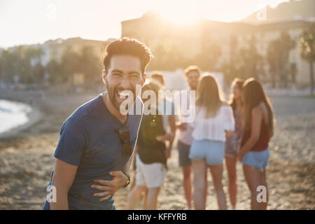 Porträt der jungen Mann, der am Strand mit Freunden lachen Stockfoto