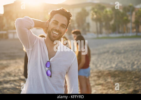 Portrait von stattlicher Mann am Strand, die Hand auf den Kopf lächelnd Stockfoto
