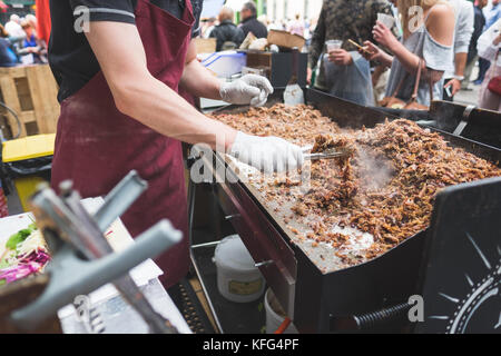 Ein Mann kochen Enten-confit auf einem offenen Grill als Menschen für ihre Nahrung, Borough Market, London warten Stockfoto
