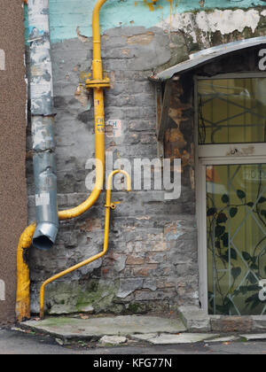 Graue Wand des Hauses mit einem alten Abflußrohr, zwei helle gelbe Wasserrohre verbogen und Kellerfenster, alte Gebäude in Kiew, Ukraine. Stockfoto