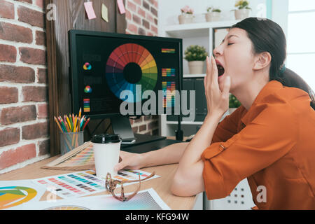 Hübsche junge Frau Designer arbeiten lange Zeit im Amt müde, gähnen und trinken heißen Kaffee zu entwerfen. Stockfoto