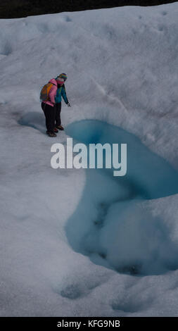 Gletscher Guide zeigt auf glazialen Pool, Abendliche auf der Oberfläche des Gletschers zu einem Pinked beschichtet weibliche Touristen auf kurze Wanderung. Stockfoto