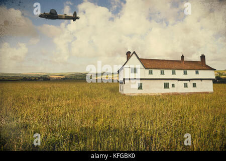 WWII Lancaster Bomber fliegen tief über ein historisches Bauernhaus, in einem ländlichen englischen Landschaft Stockfoto