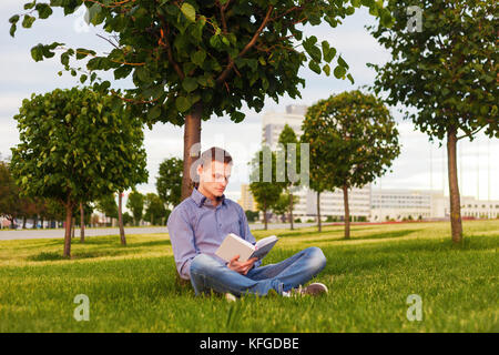 Student ein Buch lesen im Park sitzen unter einem Baum auf dem Gras. Stockfoto