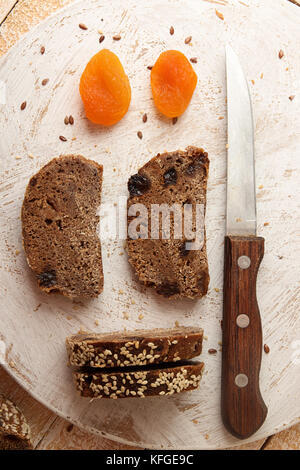 Roggenscheiben ungesäuertes Brot ohne Hefe mit getrockneten Aprikosen und Rosinen bestreuten Samen von Flachs und Sesam auf Holzbrett. Draufsicht Stockfoto