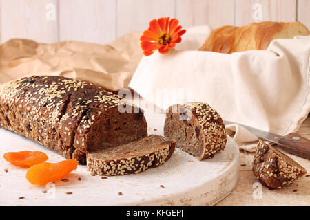 Laib und Roggenscheiben ungesäuertes Brot ohne Hefe mit getrockneten Aprikosen und Rosinen gesprinklerten Samen von Flachs und Sesam. Gesundes Lebensmittelkonzept Stockfoto