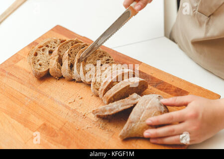 Frau Schneiden von Brot Ciabatta mit Messer in der Küche Stockfoto