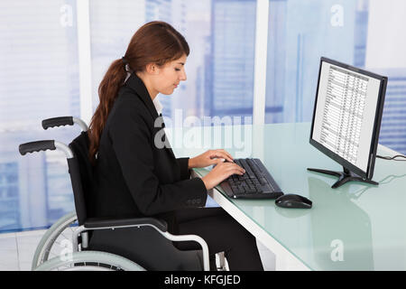 Seite Ansicht Porträt von Behinderten Geschäftsfrau mit Computer sitzend auf Rollstuhl im Büro Stockfoto