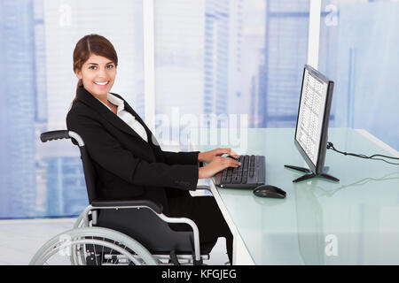 Seite Ansicht Porträt von Behinderten Geschäftsfrau mit Computer sitzend auf Rollstuhl im Büro Stockfoto