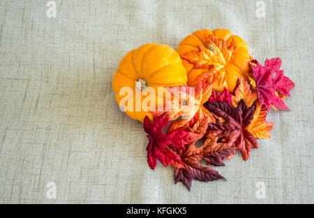 2 kleine Kürbisse mit bunten Herbstlaub auf einem braunen Tuch Hintergrund abgedeckt Stockfoto