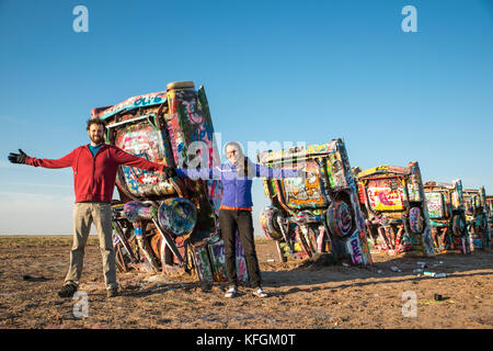 Amarillo, Texas, USA. Oktober 2015. Ein erwachsenes Paar mit offenen Armen vor einer Reihe bemalter, begrabener Autos auf der Cadillac Ranch Stockfoto